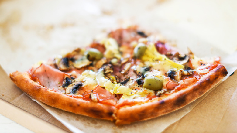 Two leftover pizza slices with meat and vegetable toppings