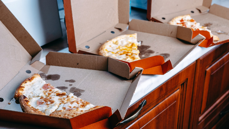 Three half pizzas in their respective pizza boxes on a counter