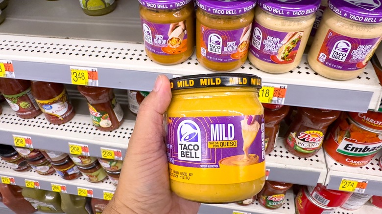 hand holding taco bell brand queso jar in supermarket