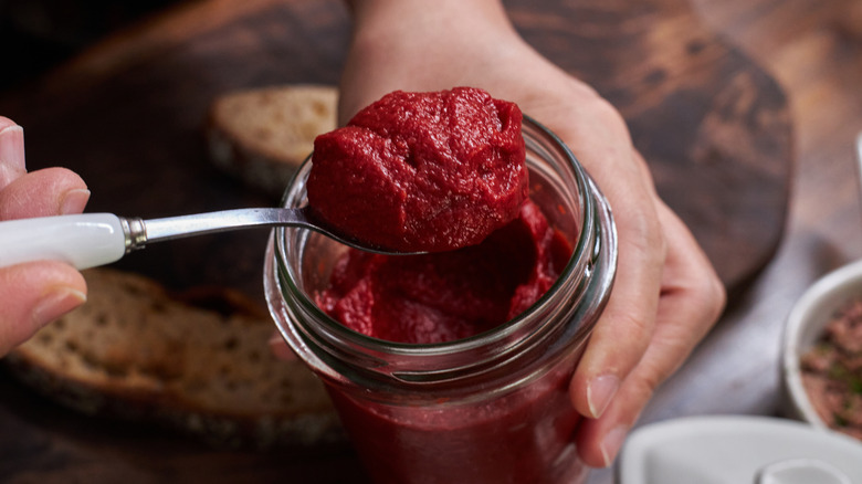 A person spooning tomato paste out of a jar