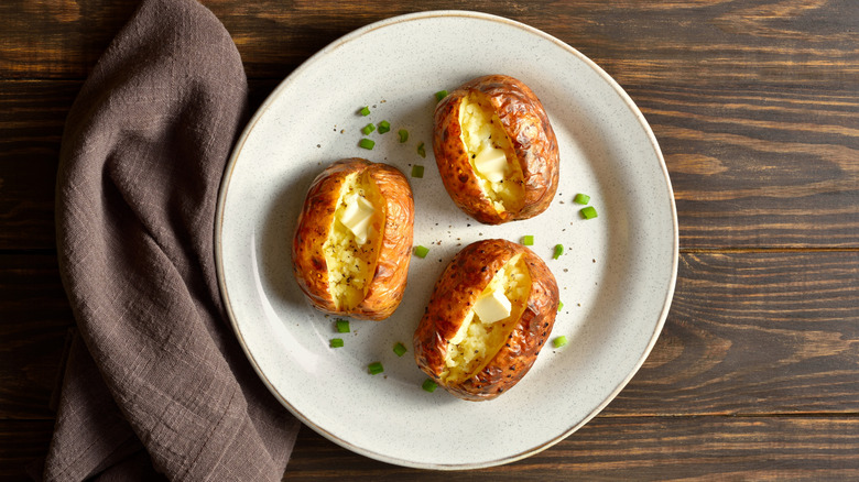 Three baked potatoes served with butter and chives on a white plate