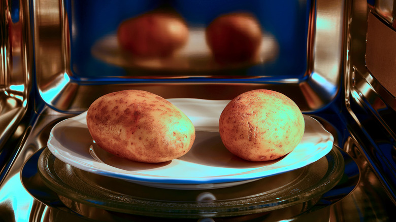 Two potatoes on a white plate in the microwave