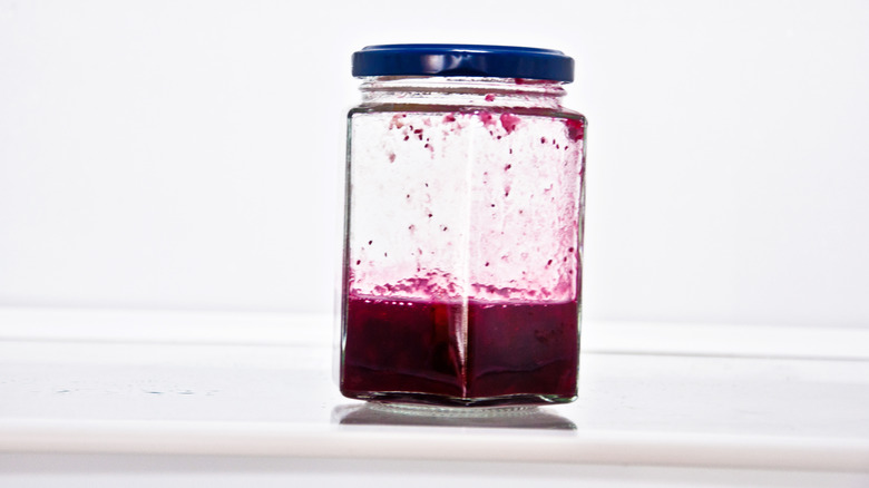 a partially full jar of jelly on a fridge shelf