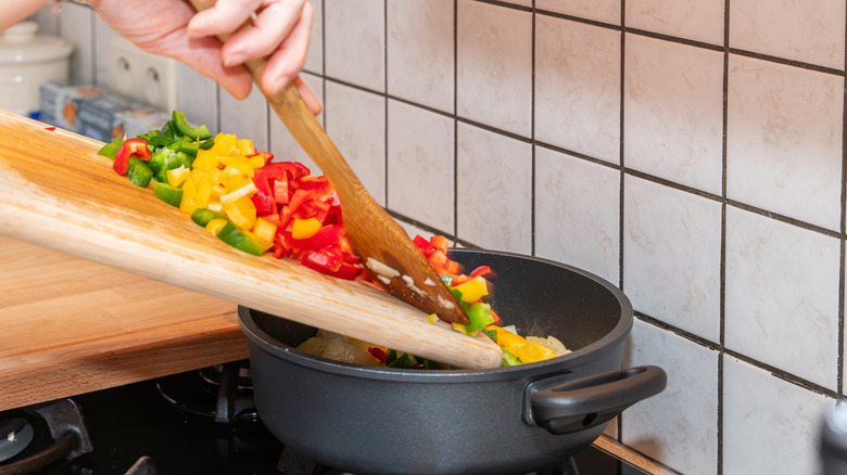 Someone putting bell peppers into a pot with a wooden spoon