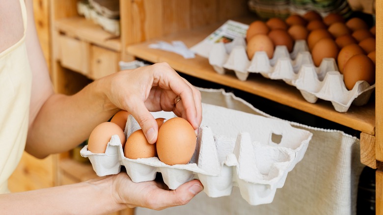 A pair of hands selects an egg from a carton of fresh eggs