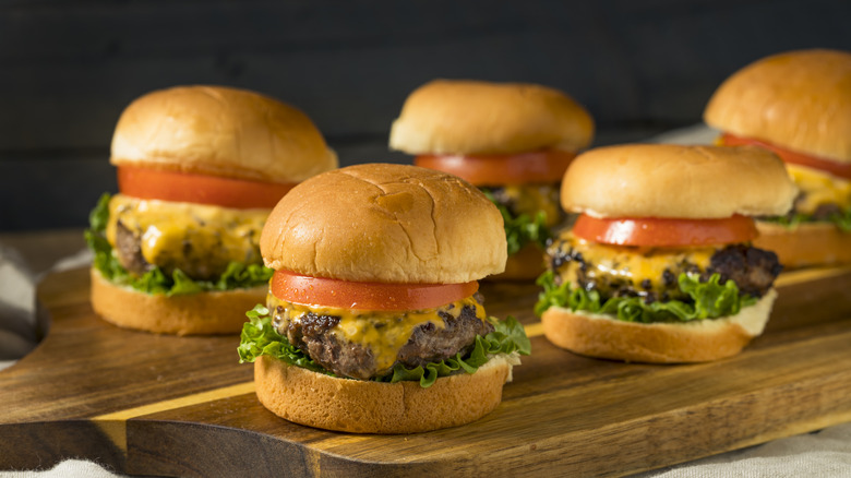 five cheeseburger sliders on a wooden cutting board