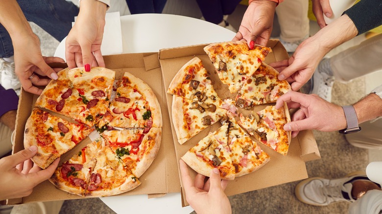 many hands reaching in for pizza slices