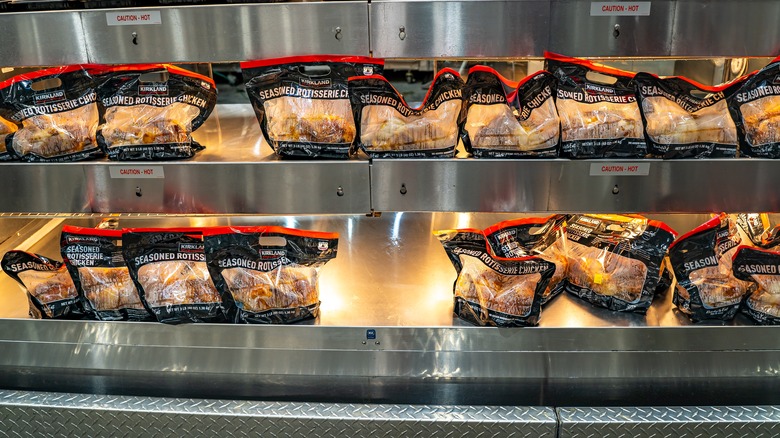 Two rows of Costco rotisserie chickens sit under heat lamps