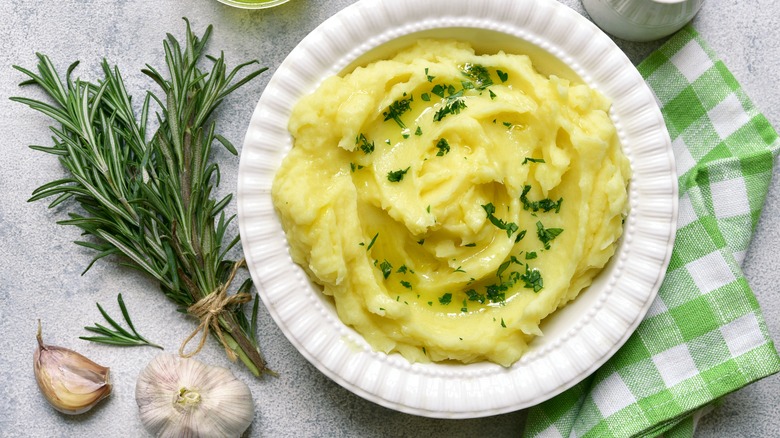 mashed potatoes garnished with rosemary in a white bowl next to a green-checked napkin