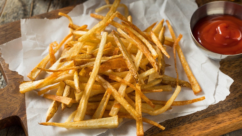 A heap of shoestring fries on paper next to a dish of ketchup