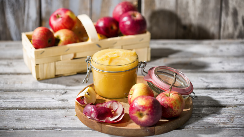 jar of applesauce with apples on wooden board