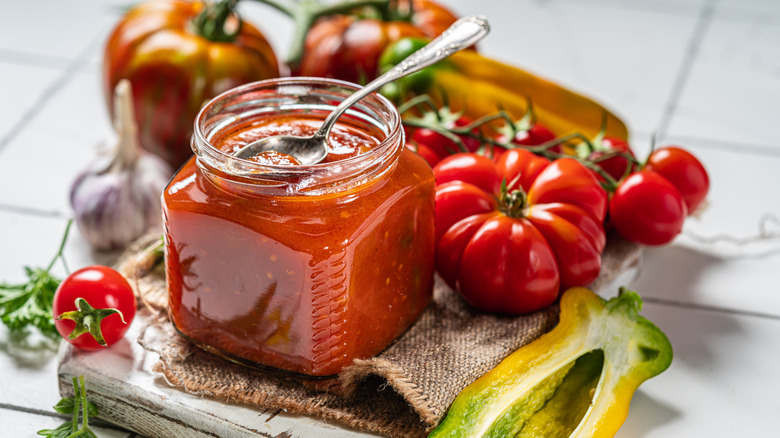 a jar of homemade salsa surrounded by tomatoes