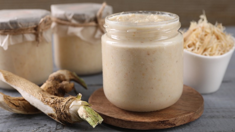 Jars of prepared horseradish next to horseradish root