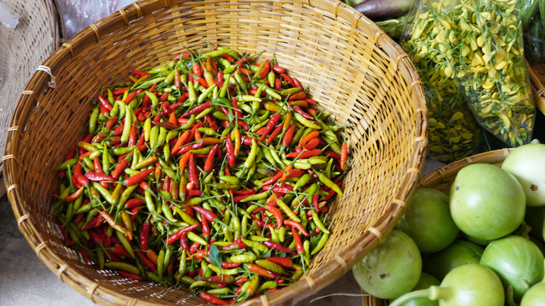 basket of various spicy Thai chili peppers surrounded by other fresh produce