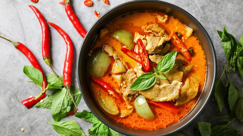 bowl of spicy Thai red curry beside red Thai chili peppers