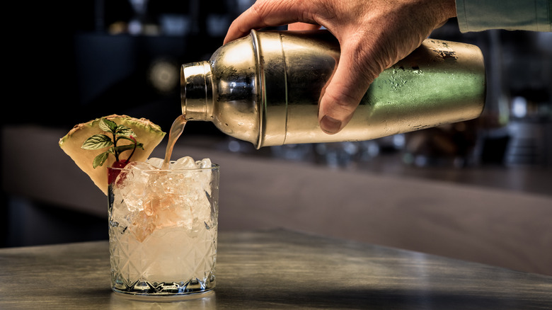 Cocktail being poured into a glass that's full of ice.