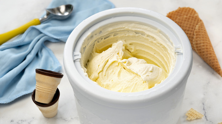 Ice cream in ice cream maker surrounded by different types of cones.