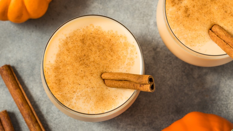 A glass of eggnog with cinnamon and cinnamon sticks.