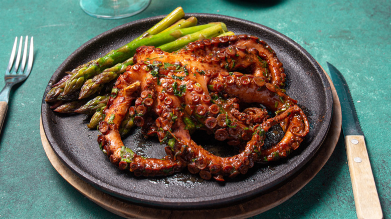 A grilled octopus served with asparagus on a plate.