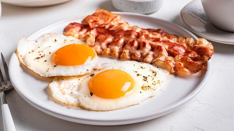 Two fried eggs and 2 slices bacon on white plate