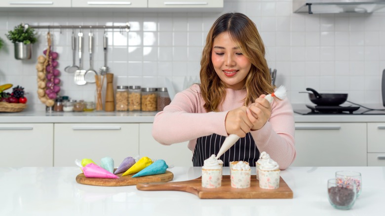 A woman decorates cupcakes with a piping bag