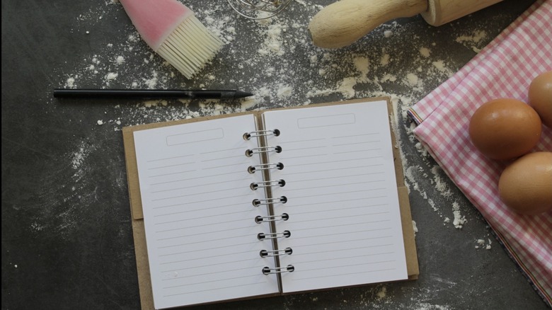 Baking utensils and eggs on a table with a notebook.