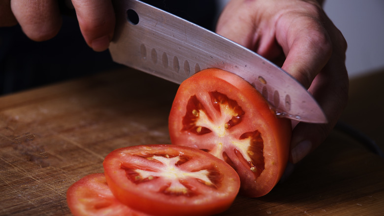 Two hands holding a knife, slicing a large tomato