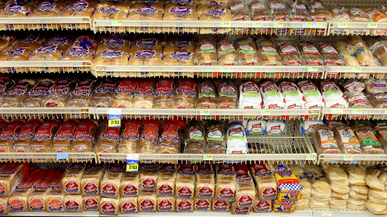 Loaves of bread sit in a grocery store aisle on tan shelves