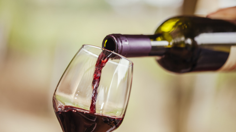 A wine glass being filled with red wine from a green glass bottle.