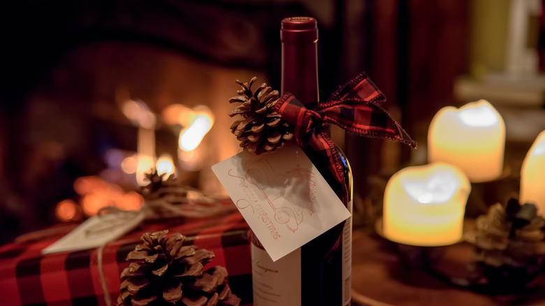 A bottle of red wine with a red ribbon and a pine cone tied around the neck