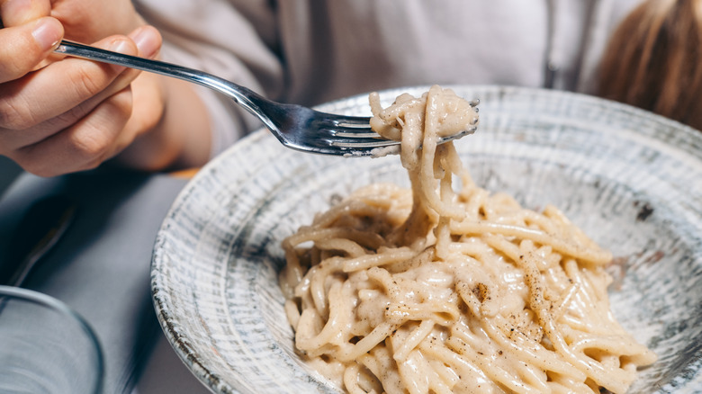 Hand holding fork over bowl with spaghetti