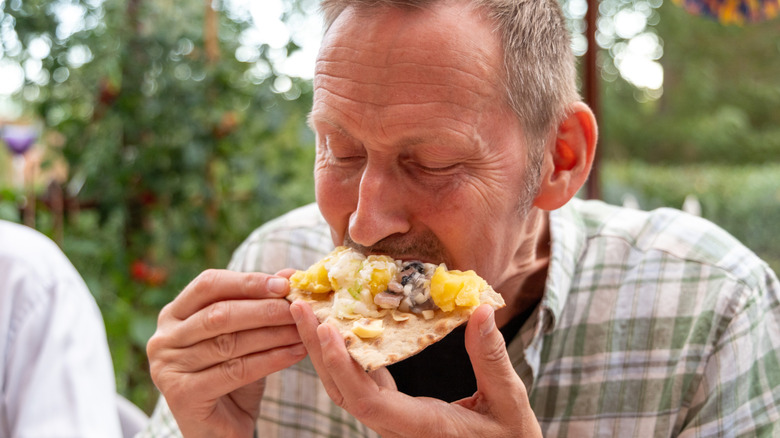 A man eating surströmming with the traditional accompaniments.