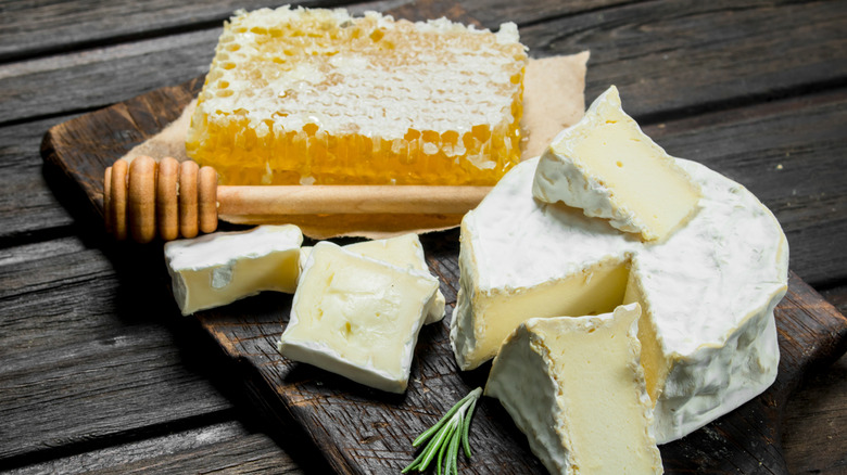 Slab of honeycomb, brie cheese and honey dipper on old wood board