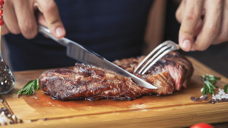 A diner cutting a steak on a wooden chopping board