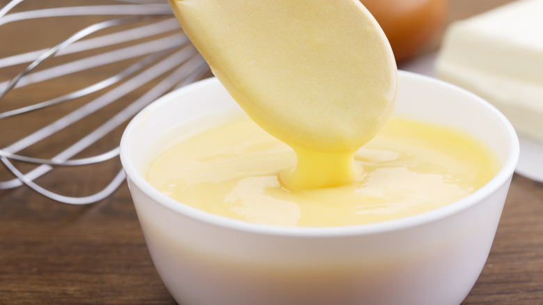 A spoon drips hollandaise sauce into a bowl