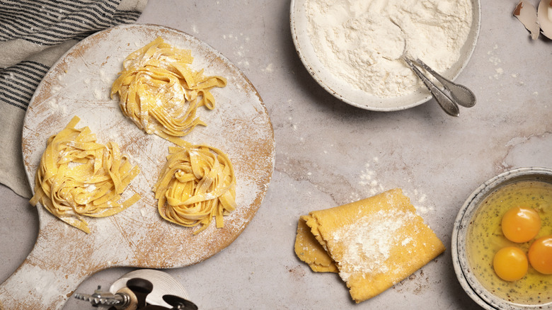 Fresh homemade pasta next to a bowl of flour and raw eggs