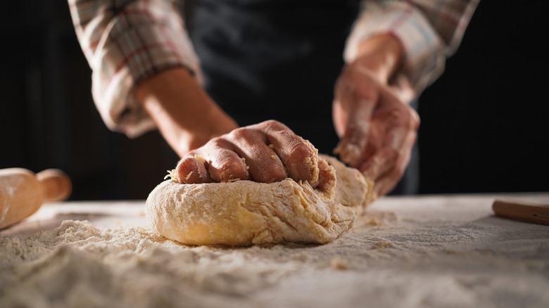 A person kneading pasta dough by hand on floured surface