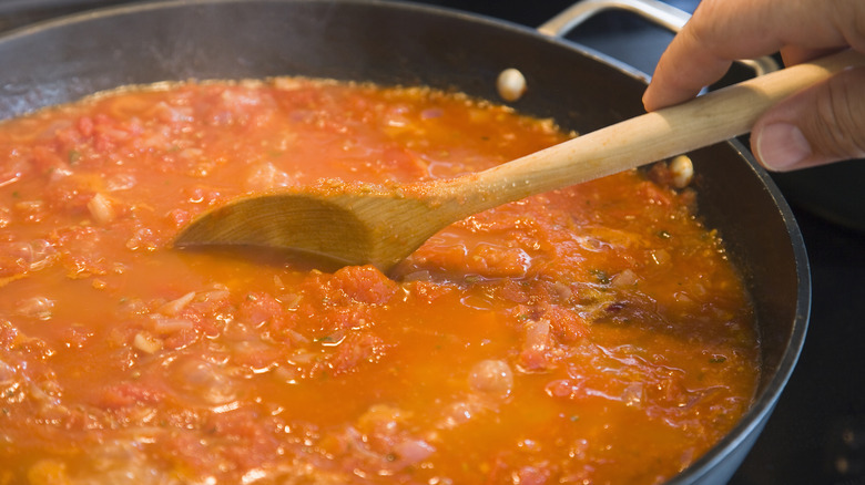 A person using a wooden spoon to stir a pot of pasta sauce