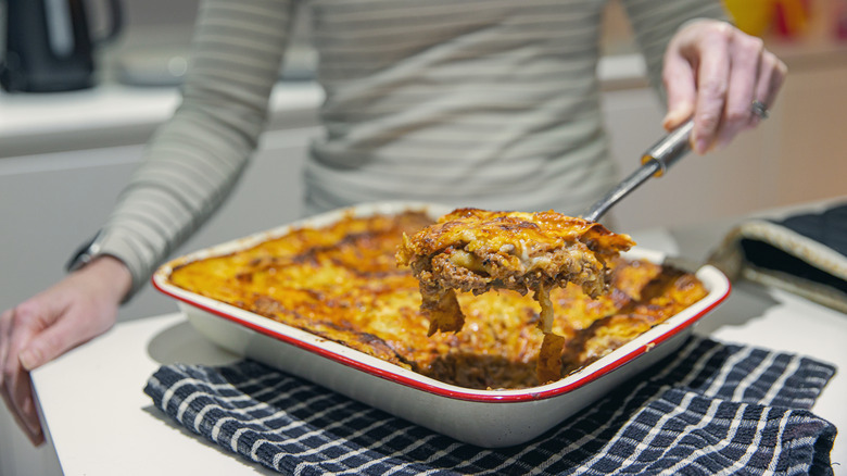 A person serving up a piece of lasagna from a square dish