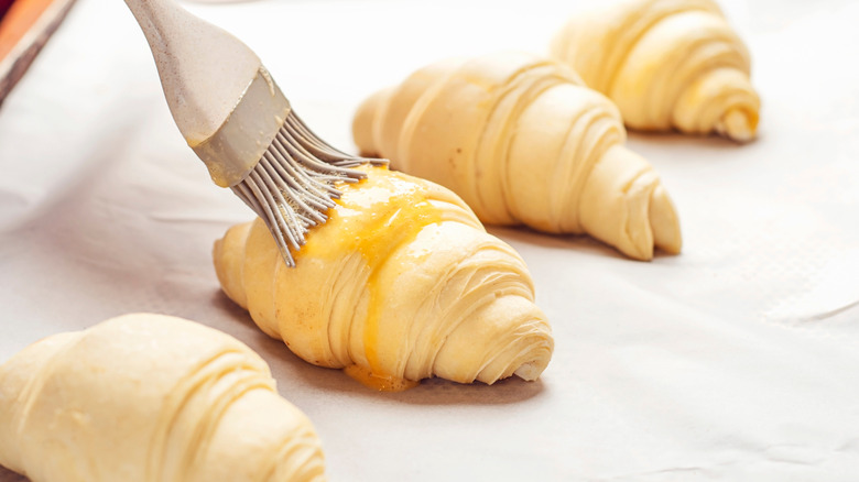 Silicone brush being used to apply egg wash to mini croissants before baking.