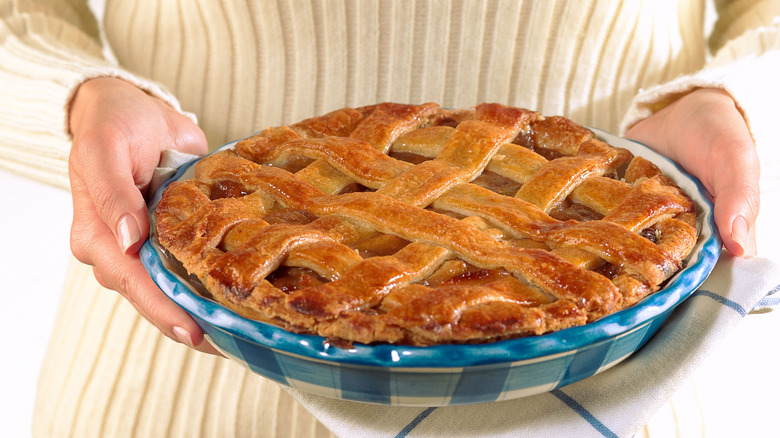 Woman in yellow knit top holding a pie in a blue serving dish.