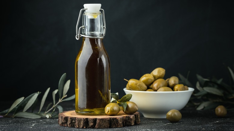 A bottle of olive oil with a bowl of green olives