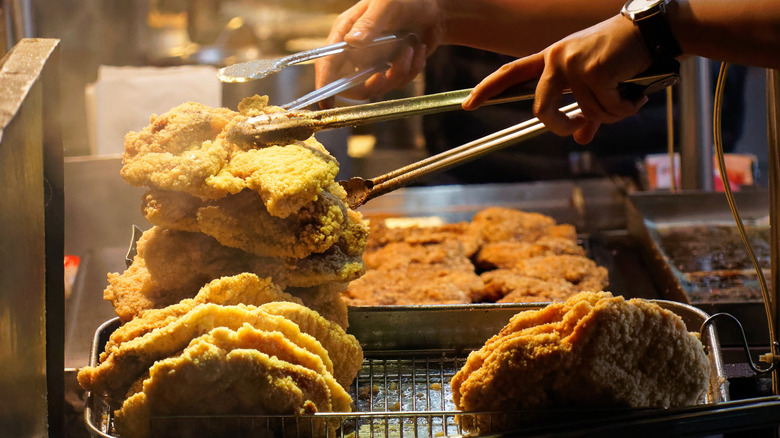 fried chicken shop employee grabbing chicken with tongs