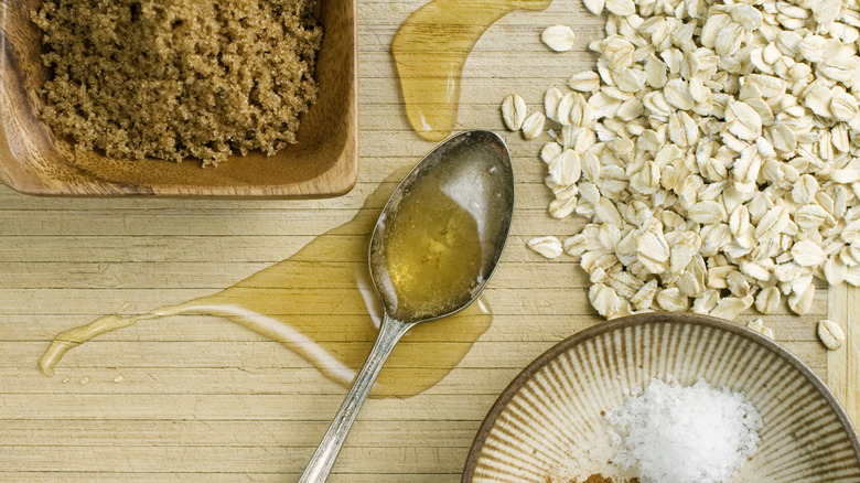 Wooden surface with a metal spoon of spilling honey alongside oats, spices, and brown sugar