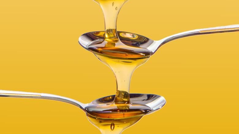 Honey falling from one spoon to the next with a yellow background