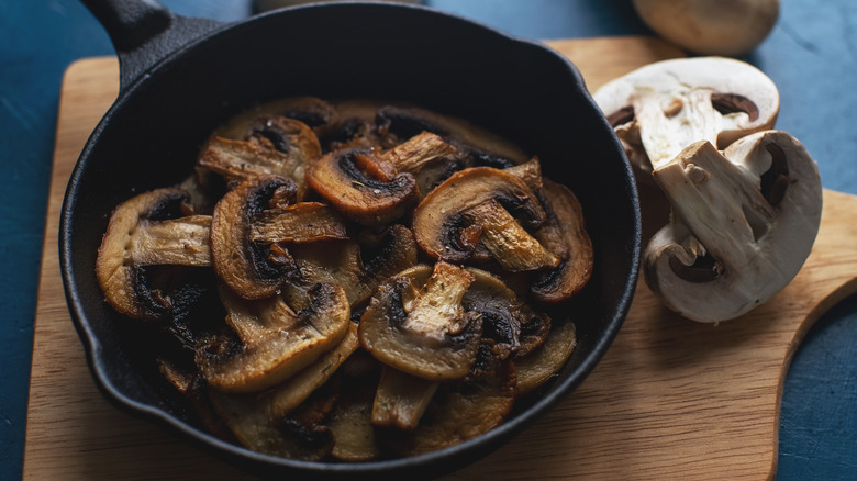 sliced mushrooms in a cast iron frying pan sitting on a wooden board