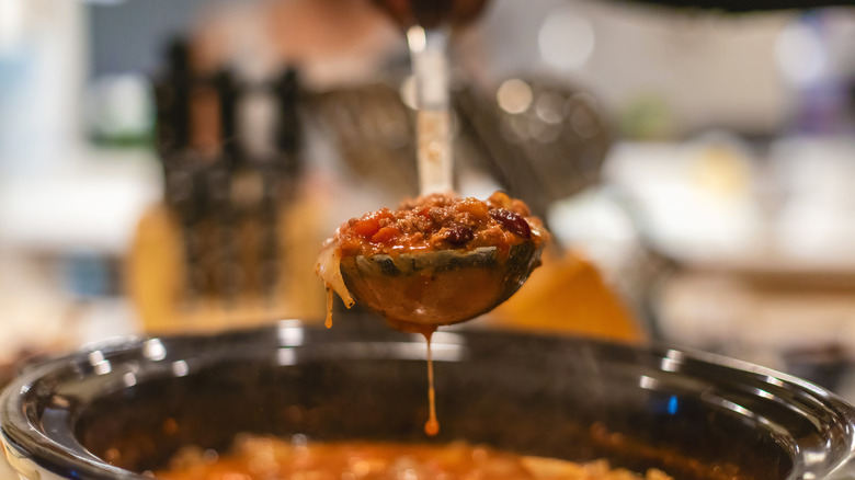 A ladle full of chili held aloft above a slow cooker