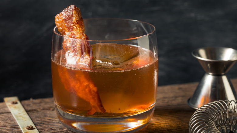 A piece of bacon sits in a glass of bourbon