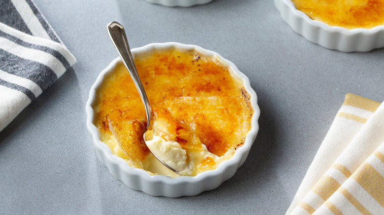 A cracked crème brûlée in a white dish with a spoon