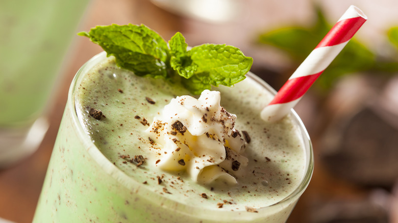 Close up of a chocolate and mint green milkshake with a spiral straw and mint leaves on top.